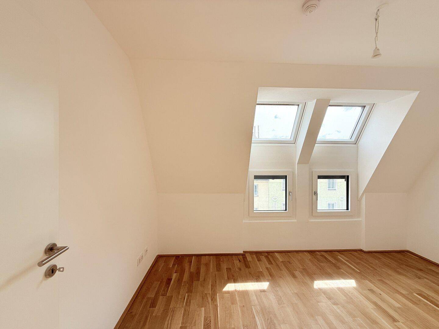 Dachzimmer mit Parkettboden und mehreren Fenstern, die einen weiten Blick ermöglichen.