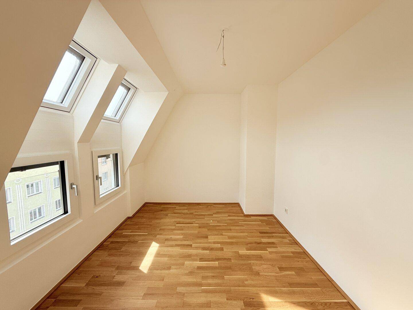 Helles Dachzimmer mit Parkettboden und schrägen Wänden, bietet eine einzigartige Wohnatmosphäre.