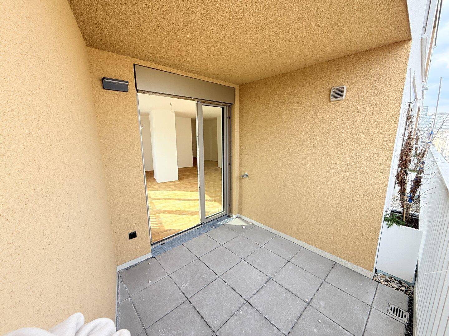 Überdachter Balkon mit Fliesenboden und Zugang zum Wohnbereich, ideal für entspannte Stunden.