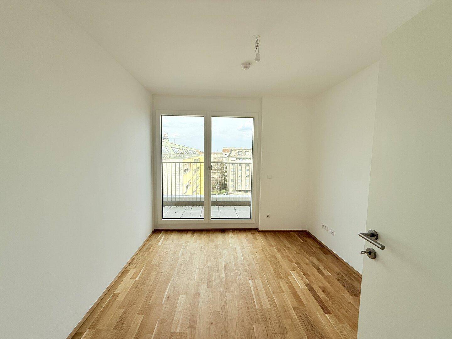Helles Schlafzimmer mit Parkettboden und großen Fenstern, bietet viel Tageslicht.
