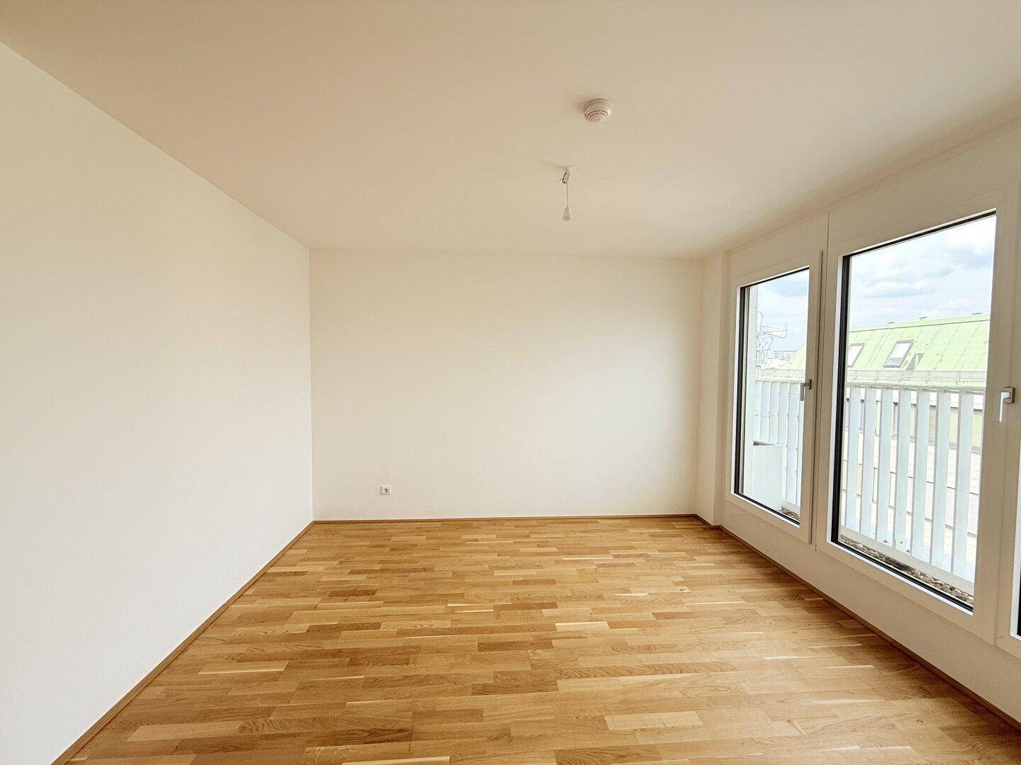 Helles Schlafzimmer mit Parkettboden und Zugang zu einem Balkon, bietet viel Tageslicht.