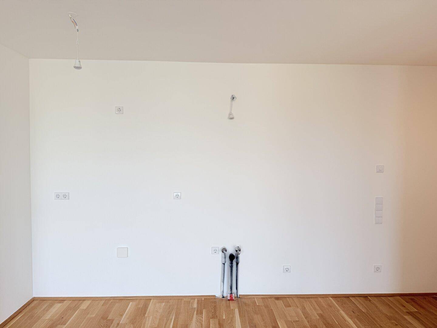 Wandbereich mit Anschlüssen für eine zukünftige Küche in einem offenen Wohnraum.