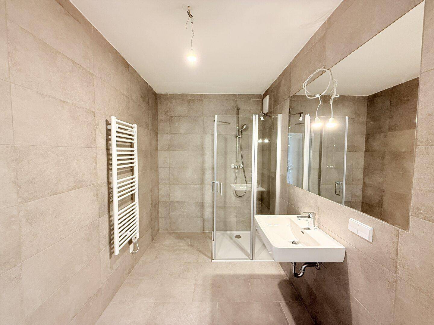 Modernes Badezimmer mit Dusche, Waschbecken, großem Spiegel und beheiztem Handtuchhalter.