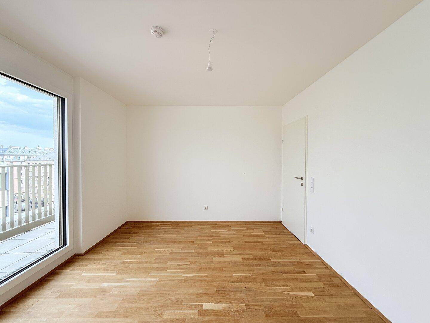 Helles Schlafzimmer mit Parkettboden und weißer Tür, bereit zur individuellen Gestaltung.