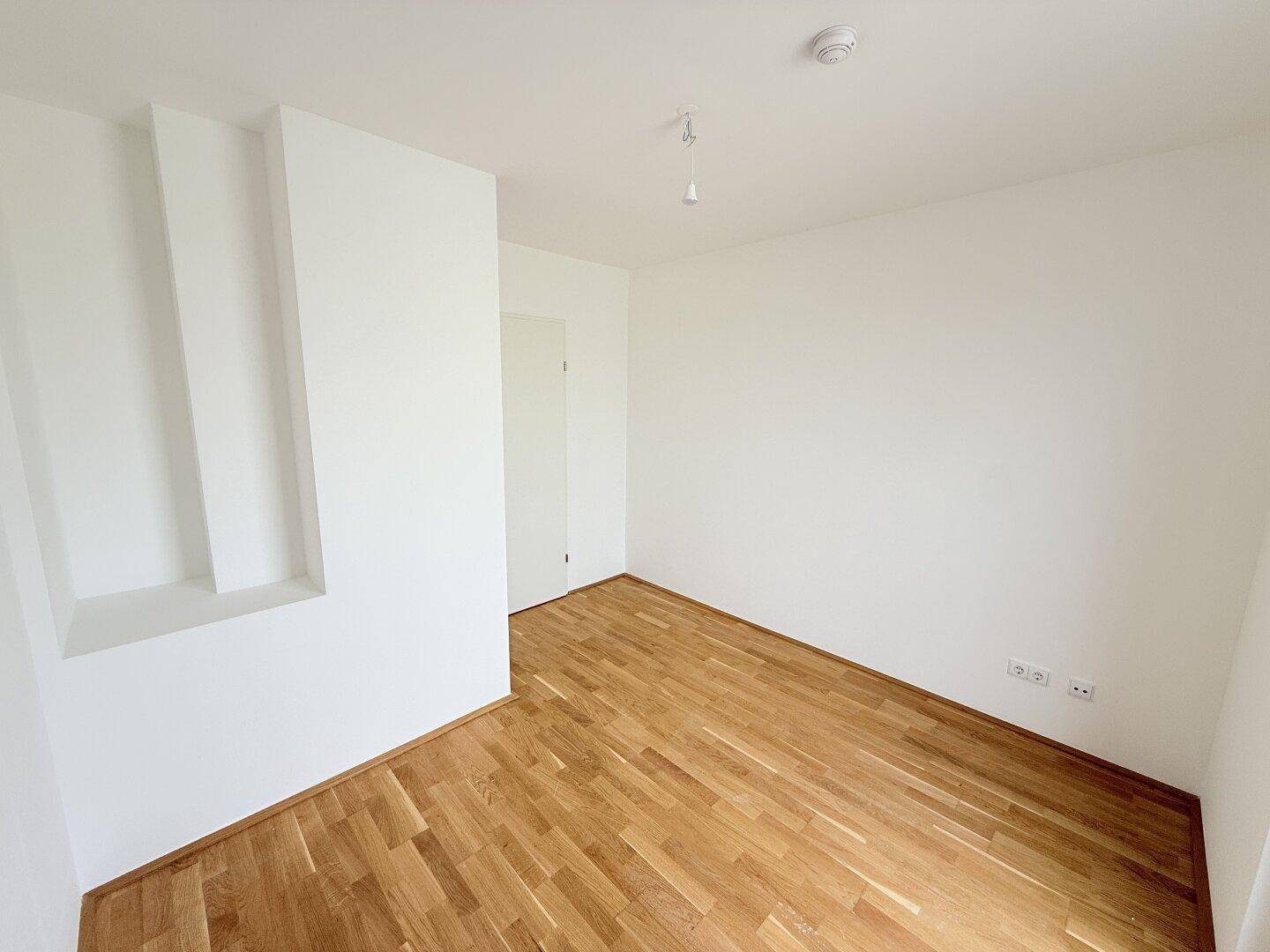 Helles Schlafzimmer mit Parkettboden und integrierter Nische, ideal für Stauraum.