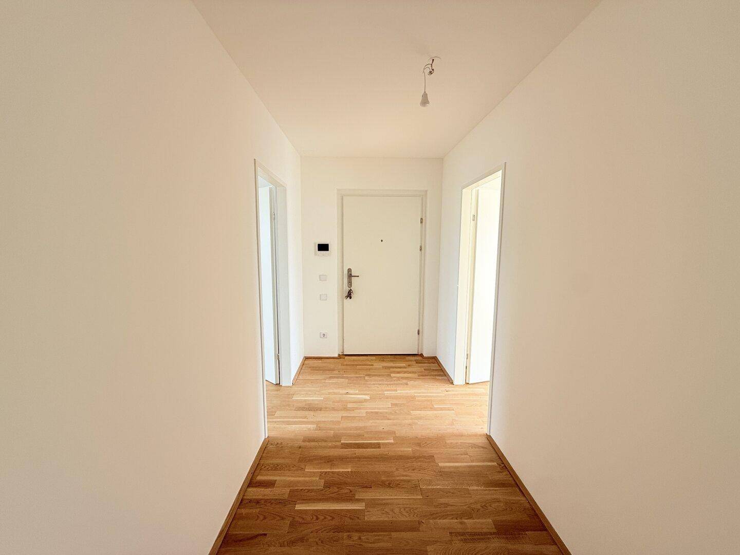 Heller Eingangsbereich mit Parkettboden und weißer Tür, führt zu den Wohnräumen.
