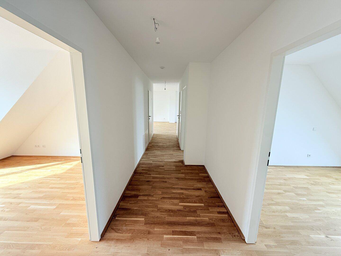 Langer, heller Flur mit Parkettboden, verbindet verschiedene Zimmer im Dachgeschoss.