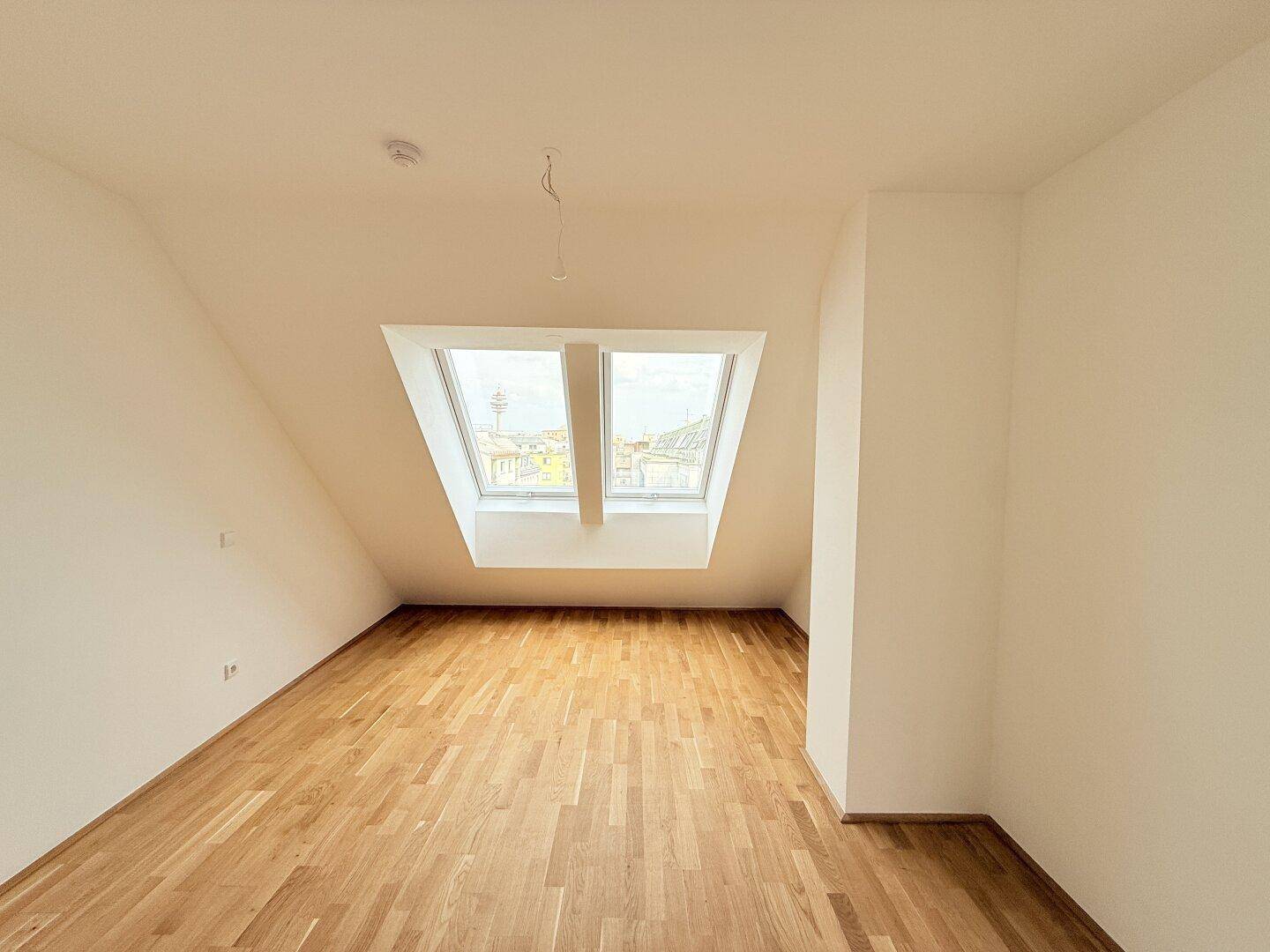 Helles Dachgeschosszimmer mit Parkettboden und zwei Dachfenstern, bietet viel Tageslicht.