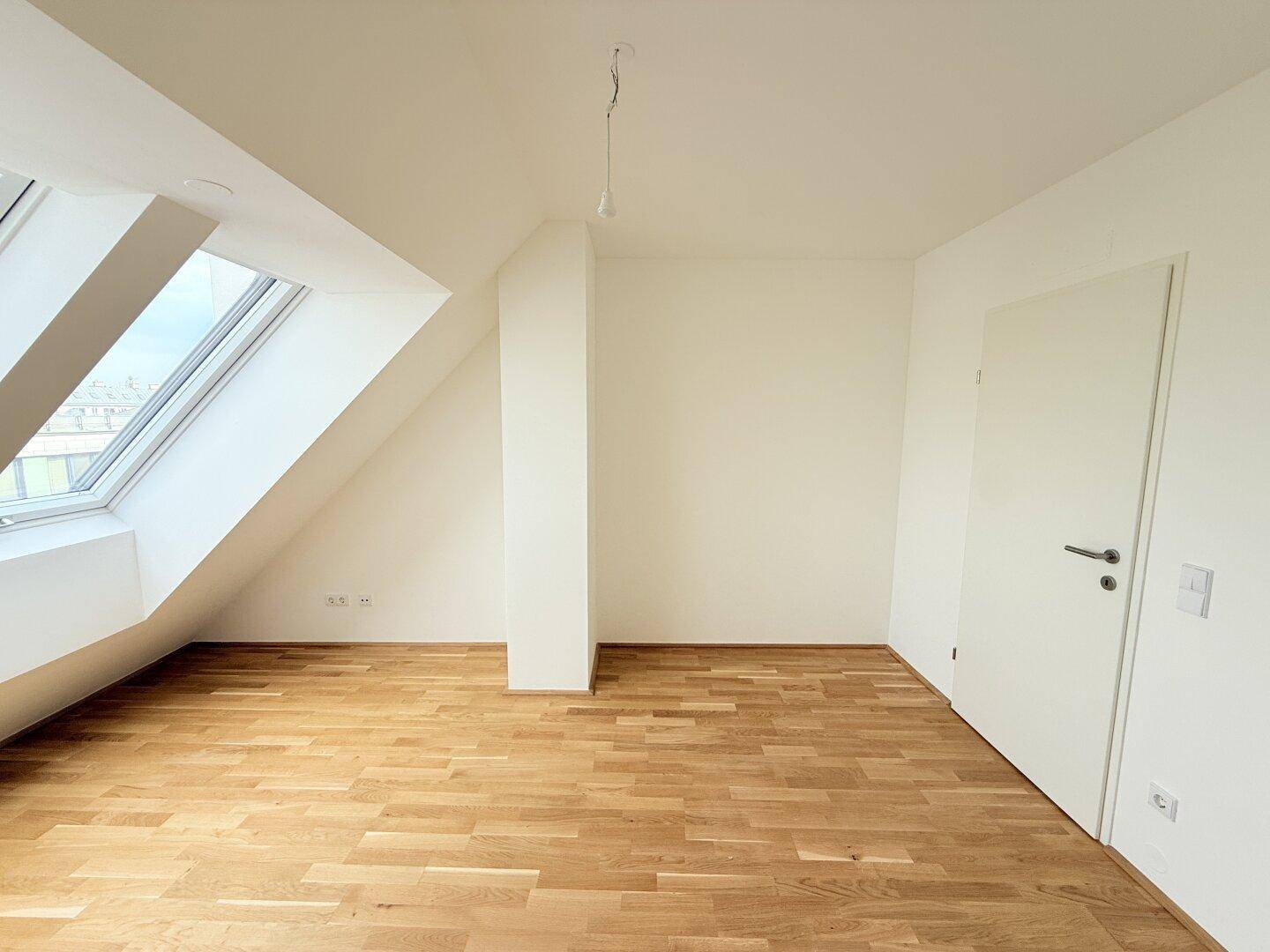 Geräumiges Dachgeschosszimmer mit Parkettboden und schrägem Dachfenster, bereit zur Einrichtung.