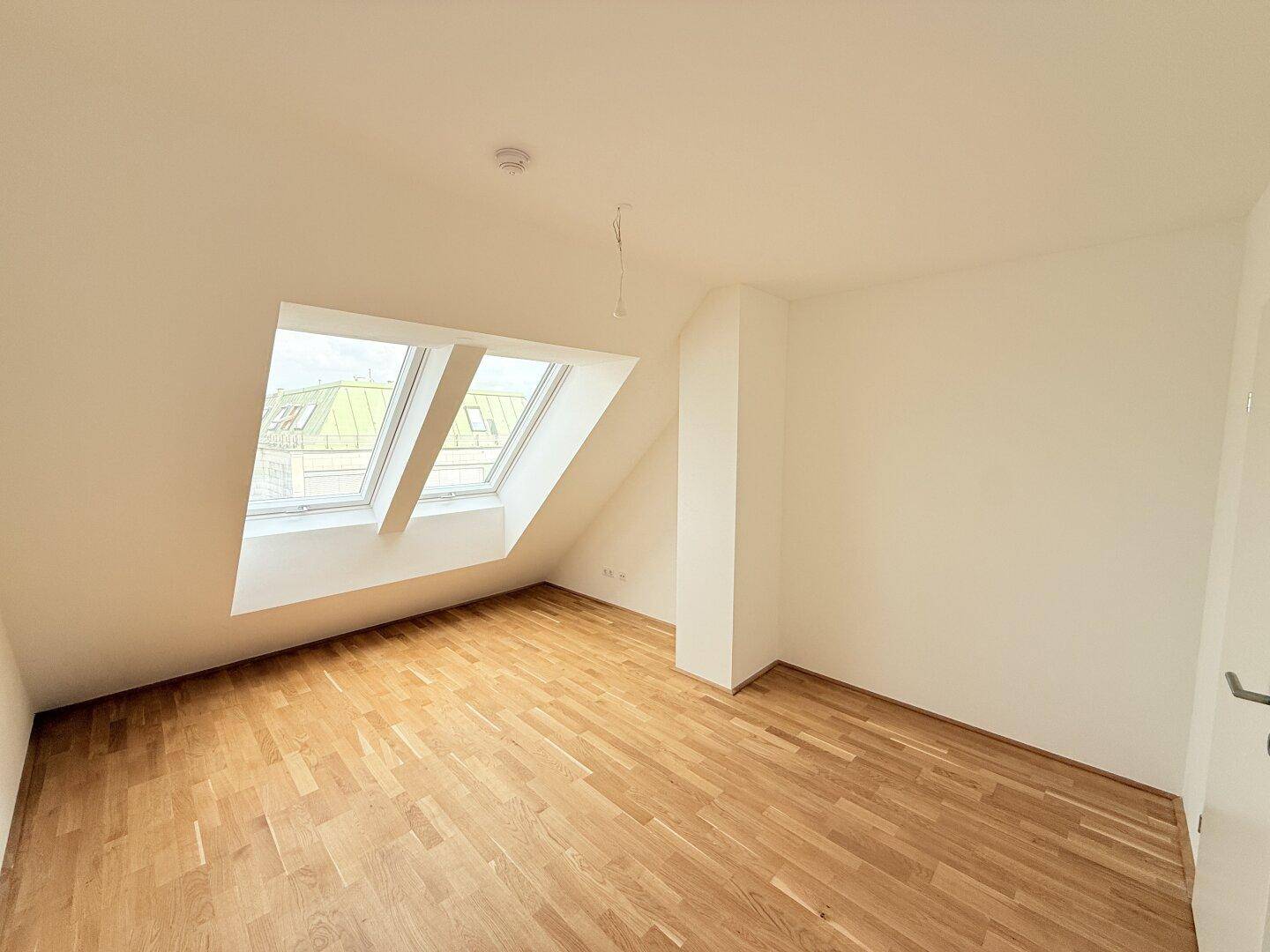 Lichtdurchfluteter Dachraum mit Parkettboden und schrägen Wänden, ideal für ein gemütliches Zuhause.