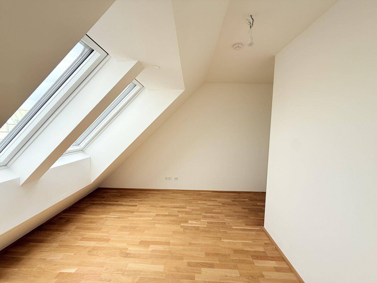 Helles Dachgeschosszimmer mit Parkettboden und schrägen Wänden, bietet viel natürliches Licht.