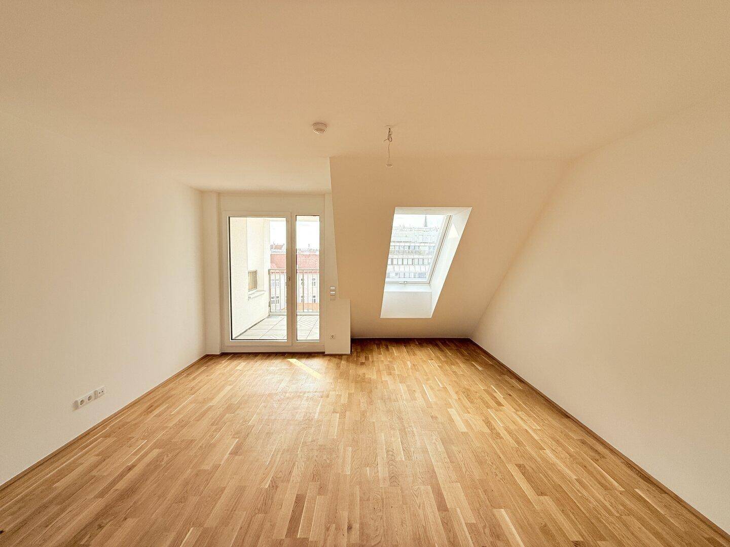 Helles Dachgeschosszimmer mit Parkettboden und Zugang zu einem Balkon, ideal für sonnige Stunden.