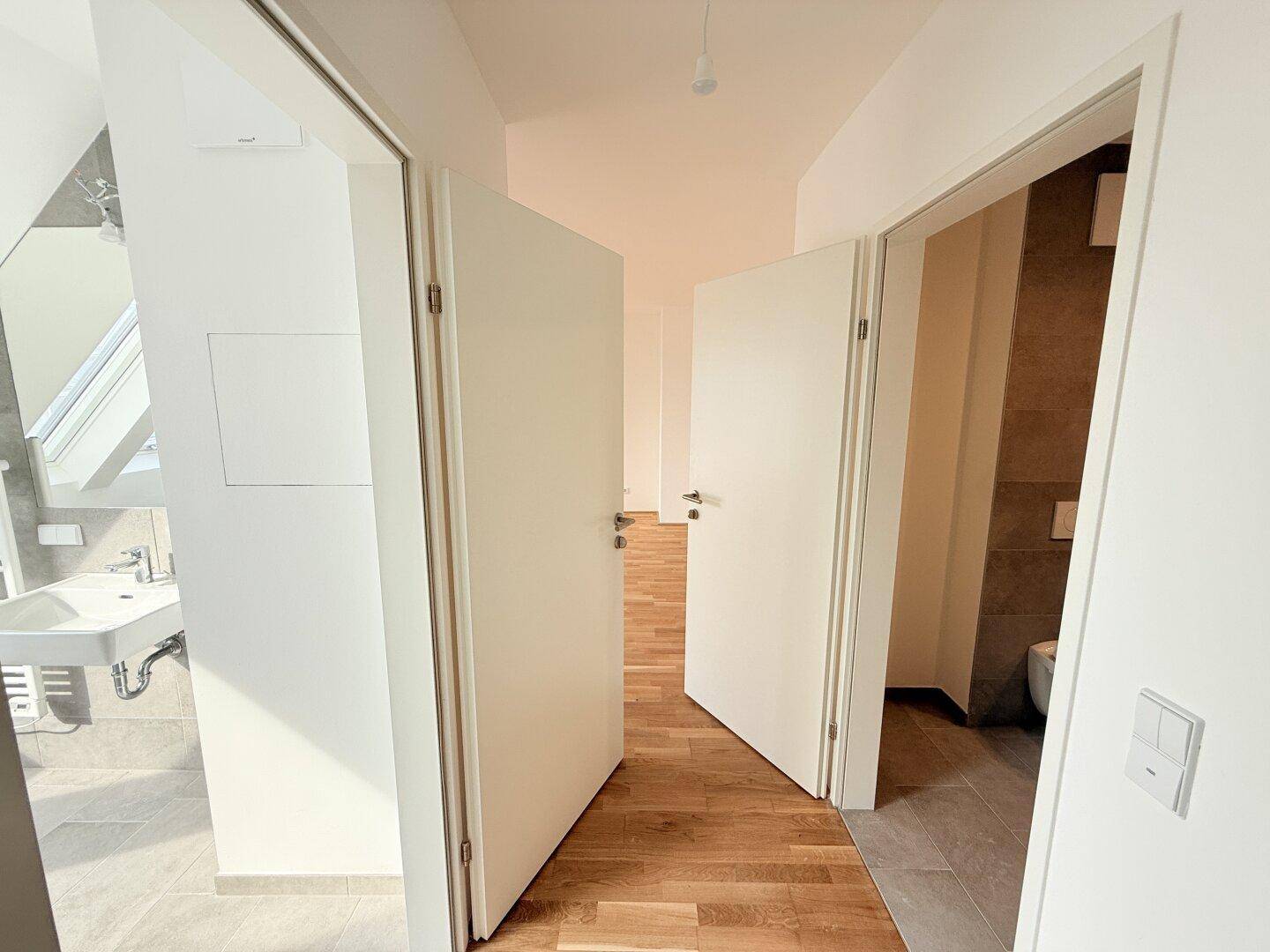 Heller Flur mit Blick auf ein modernes Badezimmer und separates WC, mit Holzboden.