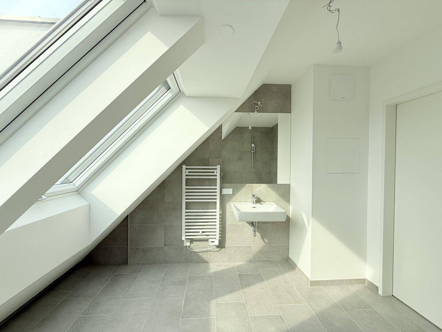 Modernes Badezimmer mit Waschbecken, beheiztem Handtuchhalter und Dachfenster, hell und funktional.