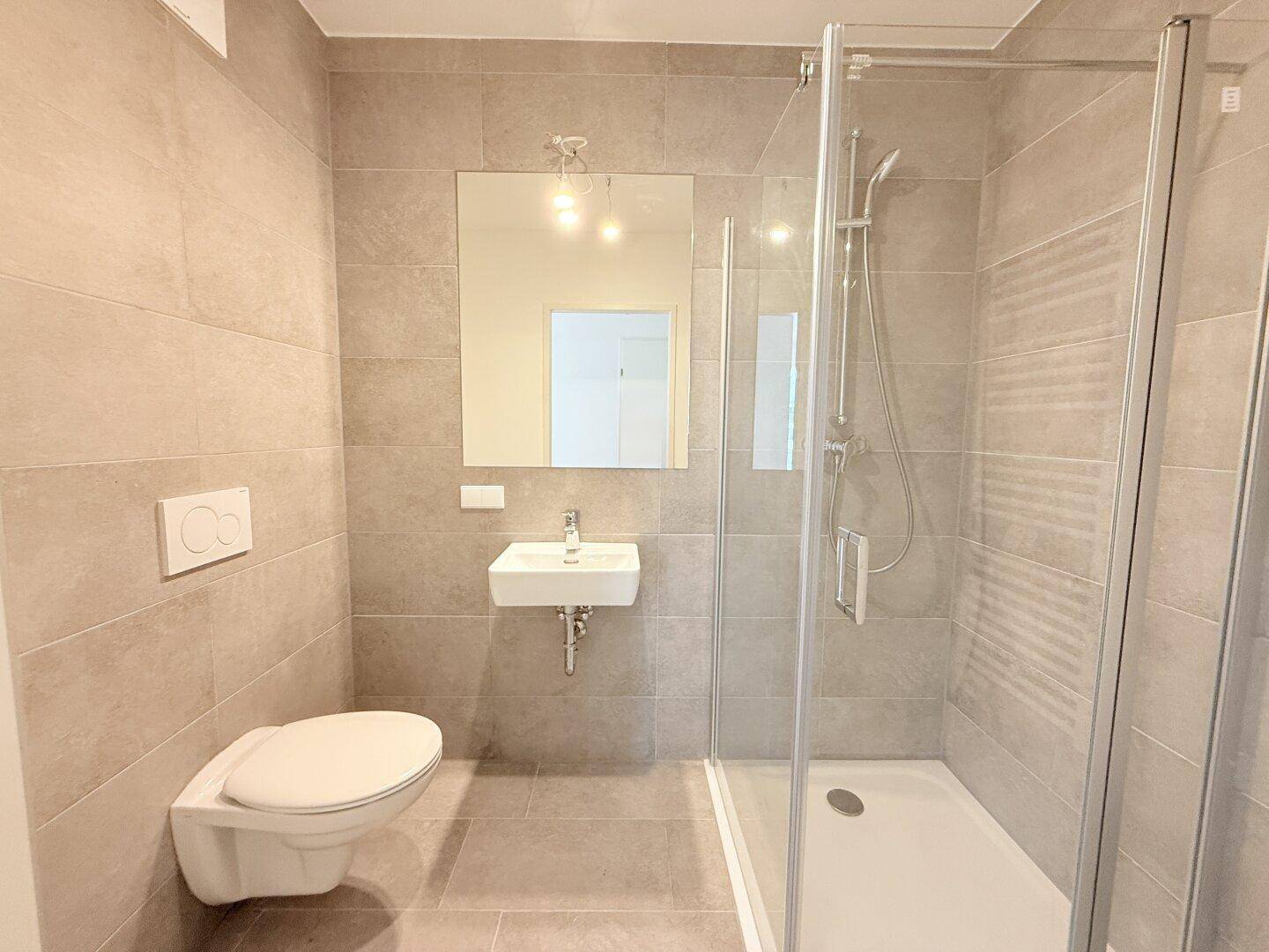 Modernes Badezimmer mit Dusche, wandhängendem WC und Waschbecken, in hellen Grautönen gefliest.