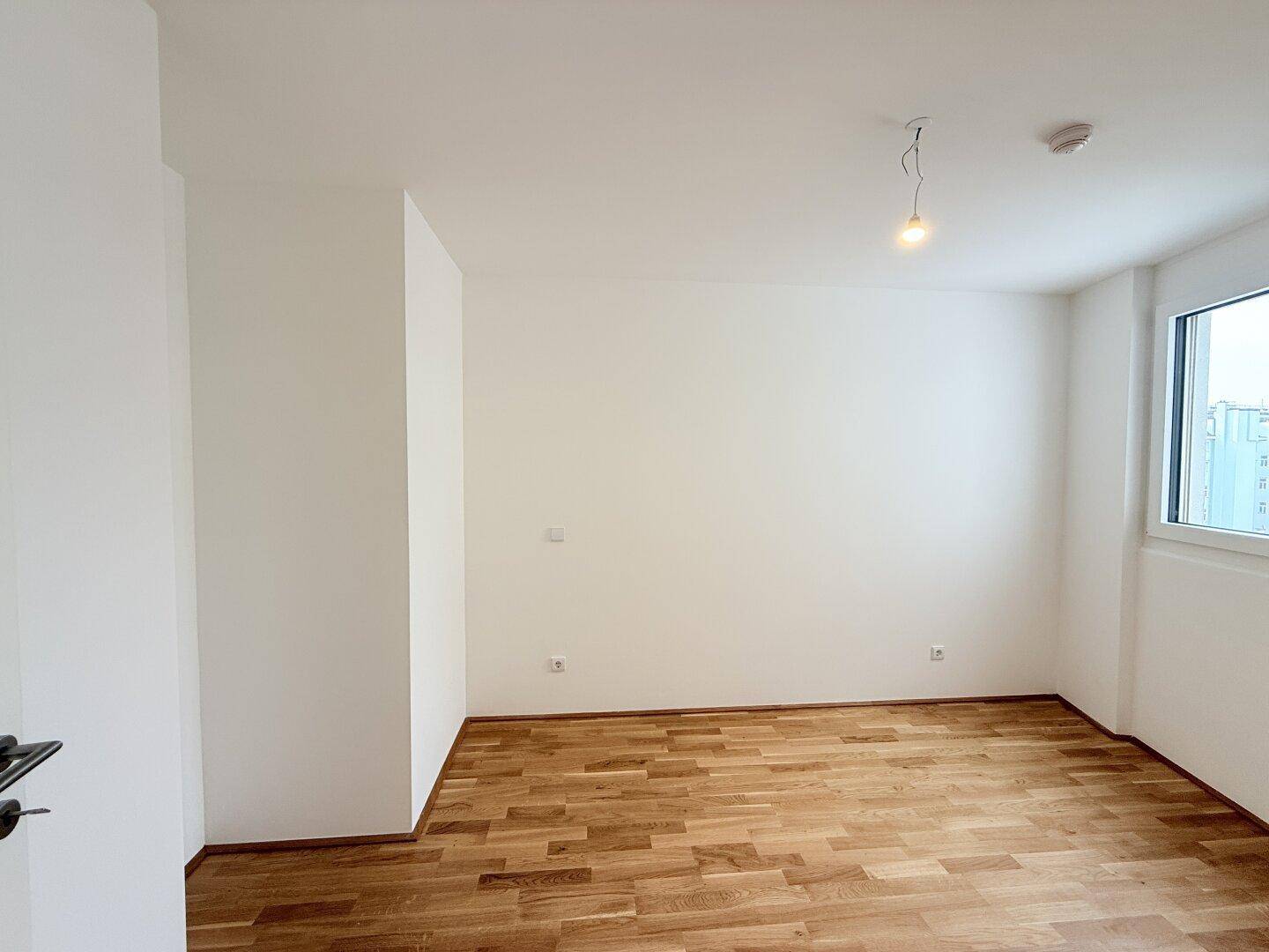 Helles Schlafzimmer mit Parkettboden und einem Fenster, das Tageslicht hereinlässt.