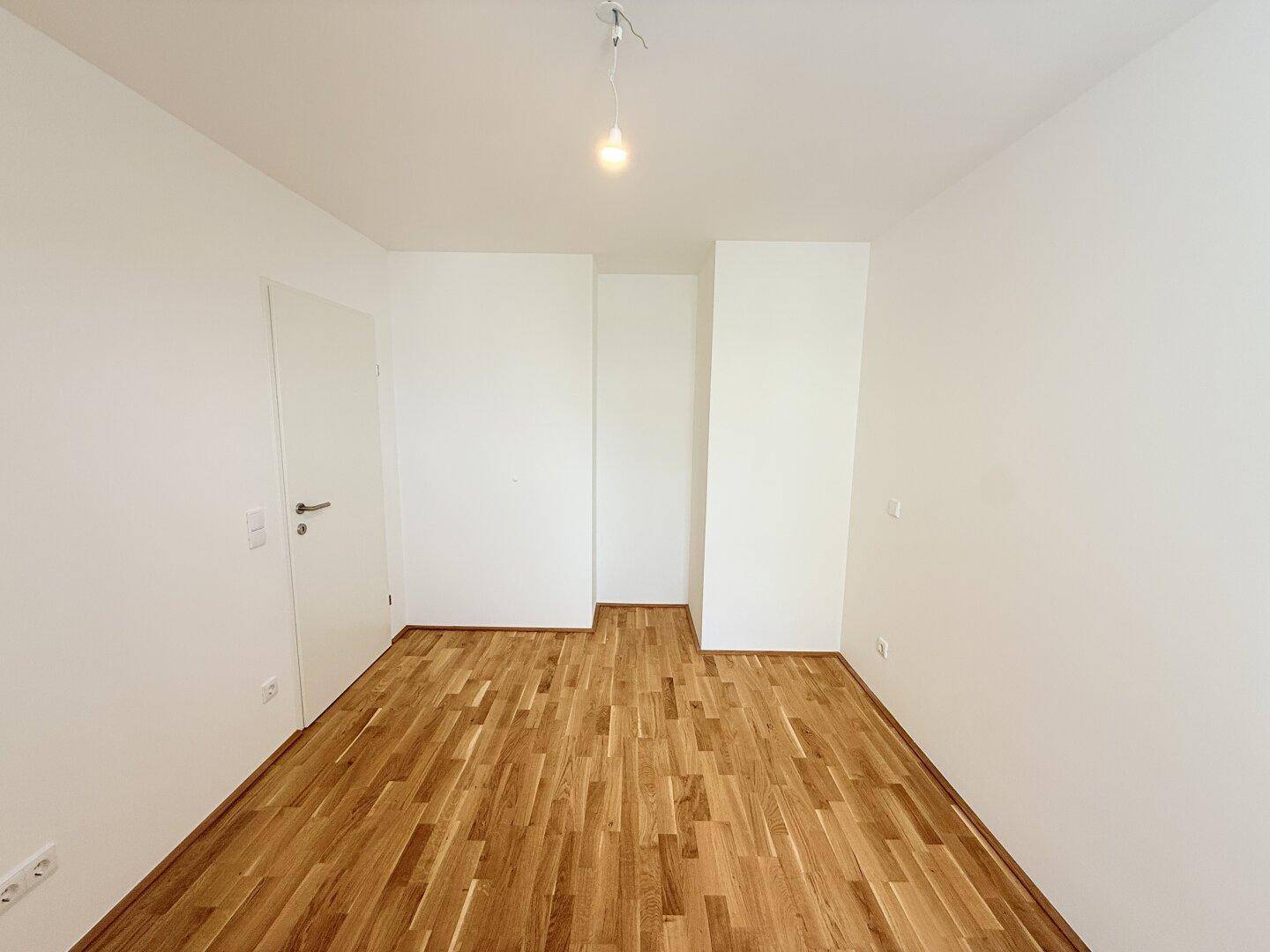 Leeres Zimmer mit Parkettboden und weißer Tür, bereit für individuelle Einrichtung.