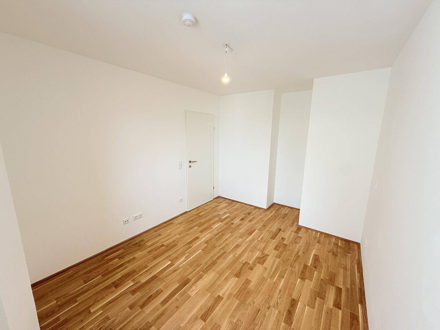 Helles Zimmer mit Parkettboden und weißer Tür, bietet eine neutrale Basis.