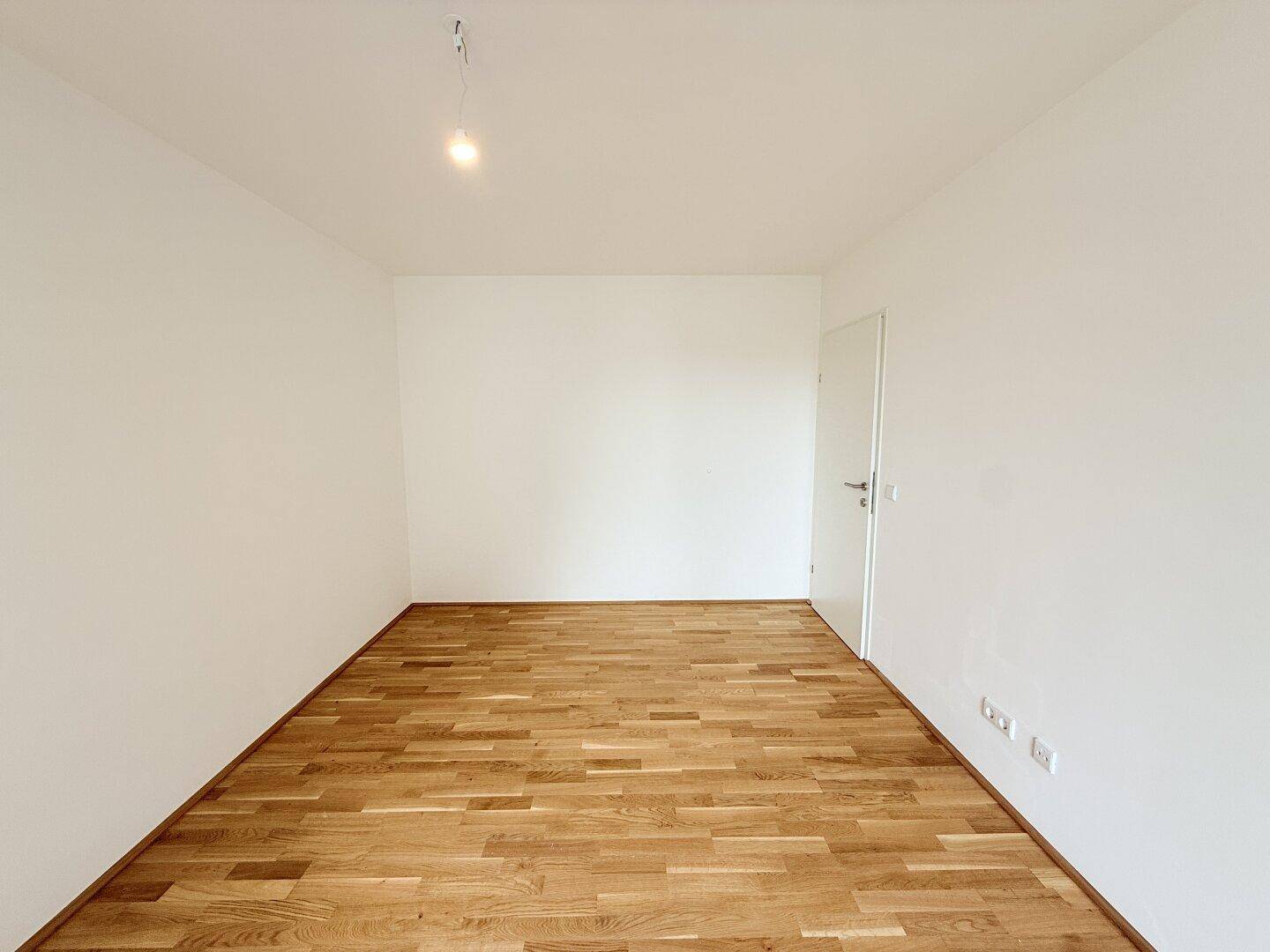 Leeres Zimmer mit Parkettboden und weißen Wänden, bereit zur individuellen Gestaltung.