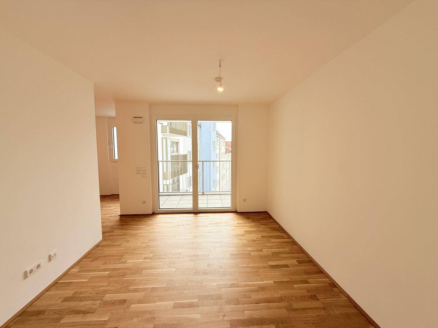 Geräumiger, heller Wohnbereich mit Holzboden und großen Fenstern zum Balkon.