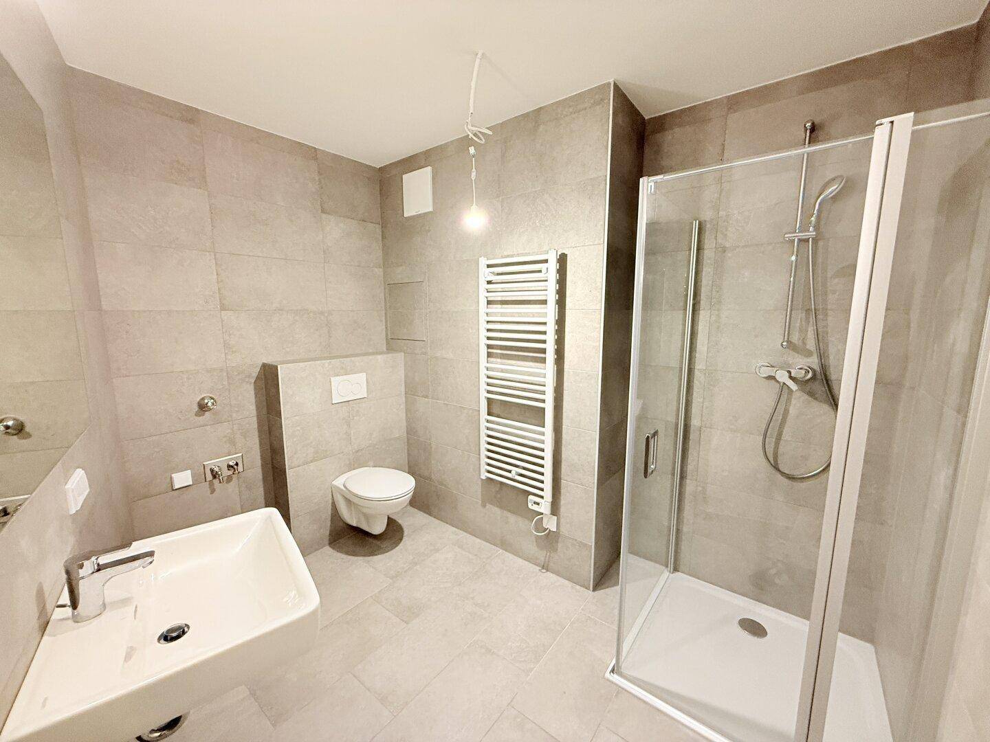 Helles Badezimmer mit modernen grauen Fliesen, Dusche, WC und Waschtisch.