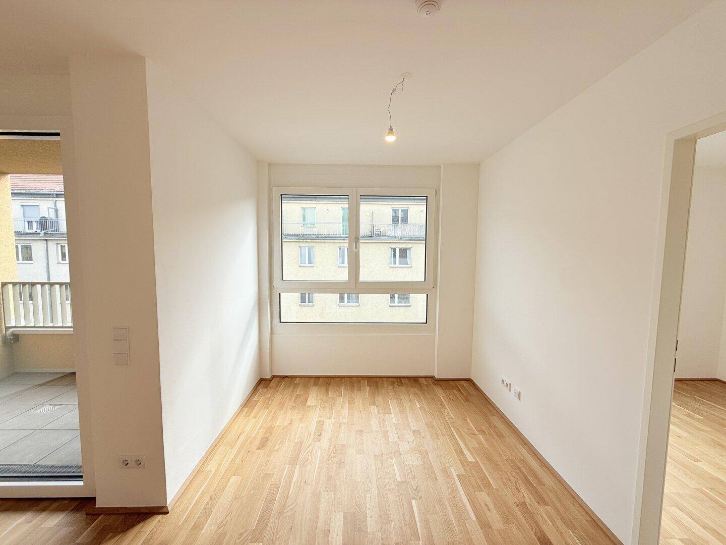 Heller Wohnraum mit großem Fenster, Parkettboden und Blick auf die umliegenden Gebäude.