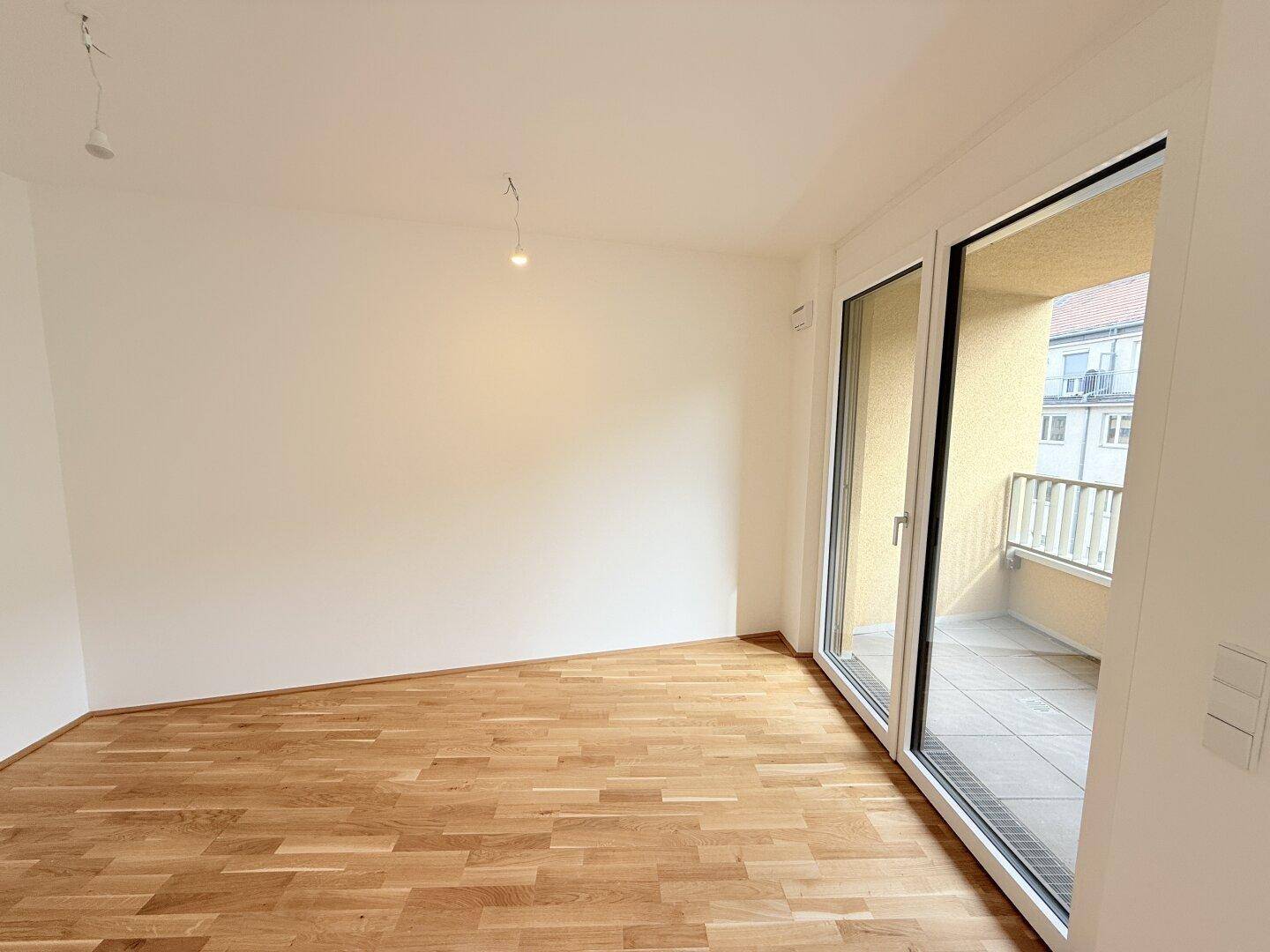 Lichtdurchfluteter Wohnraum mit Parkettboden und direktem Zugang zu einem sonnigen Balkon.