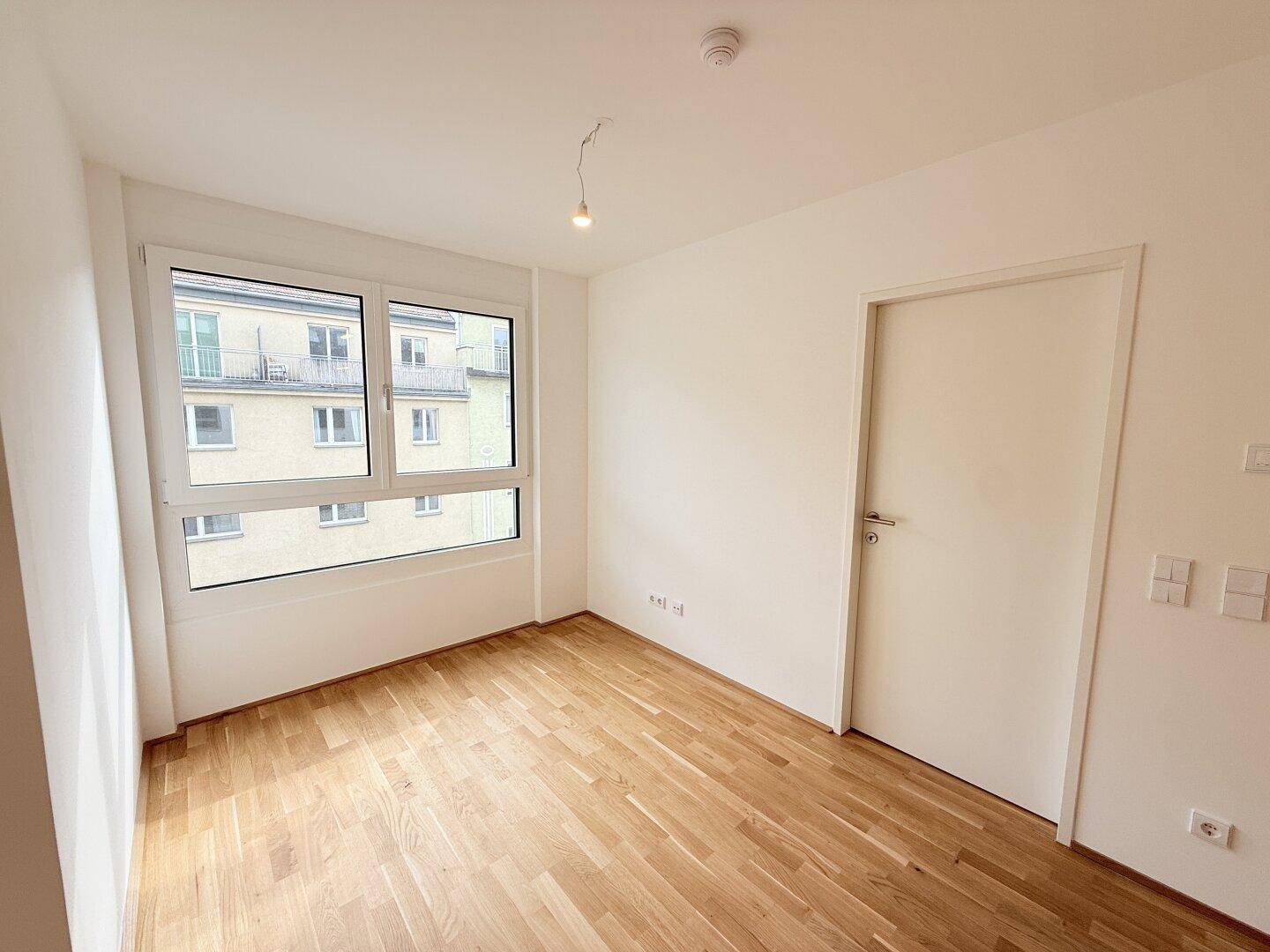 Unmöbliertes Schlafzimmer mit Parkettboden, Fenster und weiß gestrichenen Wänden, bereit zur Einrichtung.