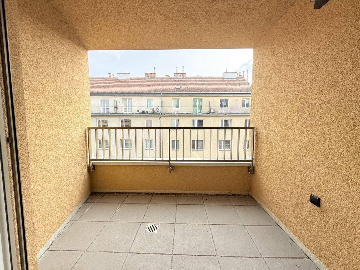Geräumiger Balkon mit Fliesenboden und Blick auf die umliegenden Stadtgebäude.