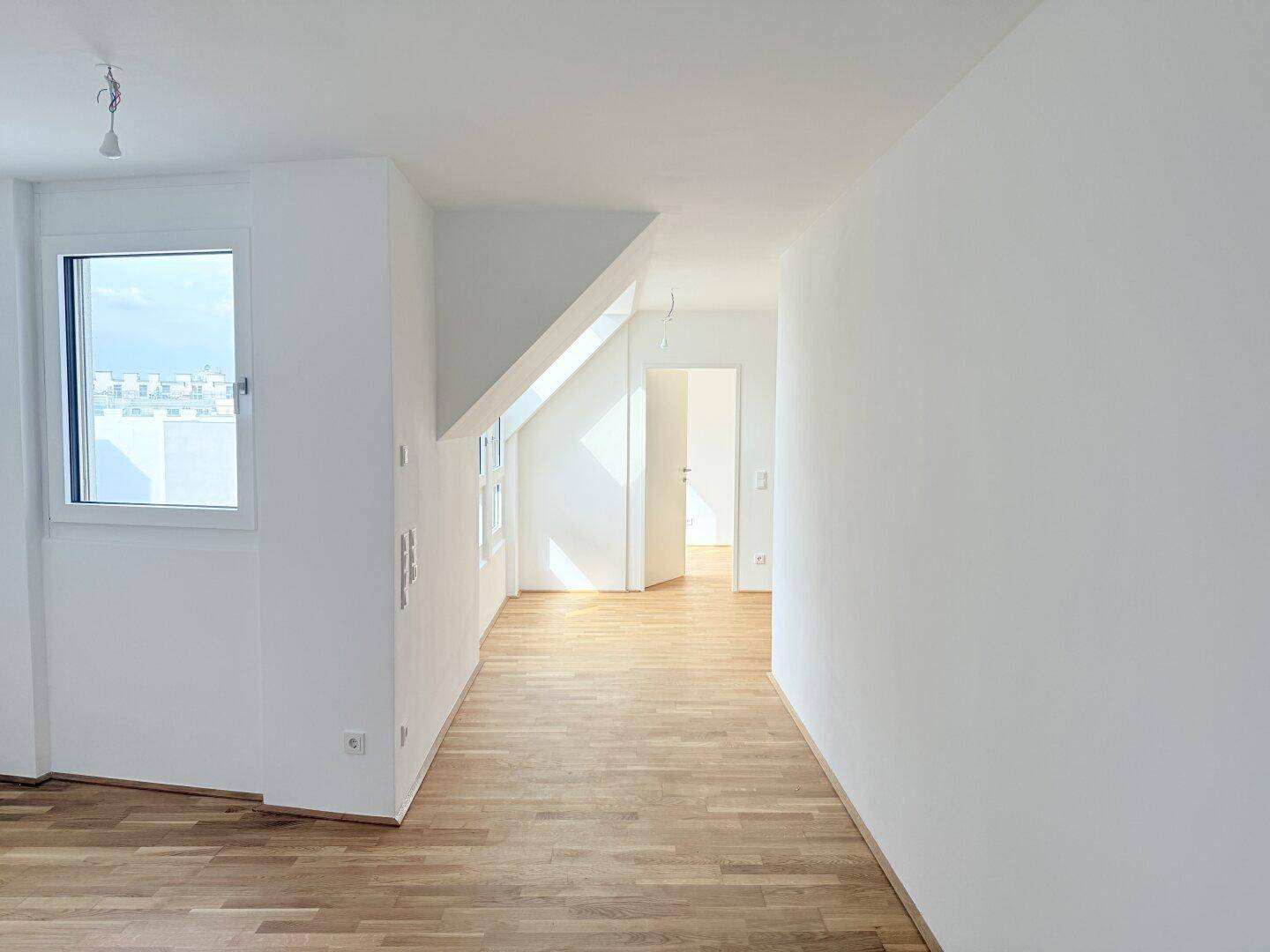 Helles Zimmer im Dachgeschoss mit schrägen Wänden, Fenster und Parkettboden.