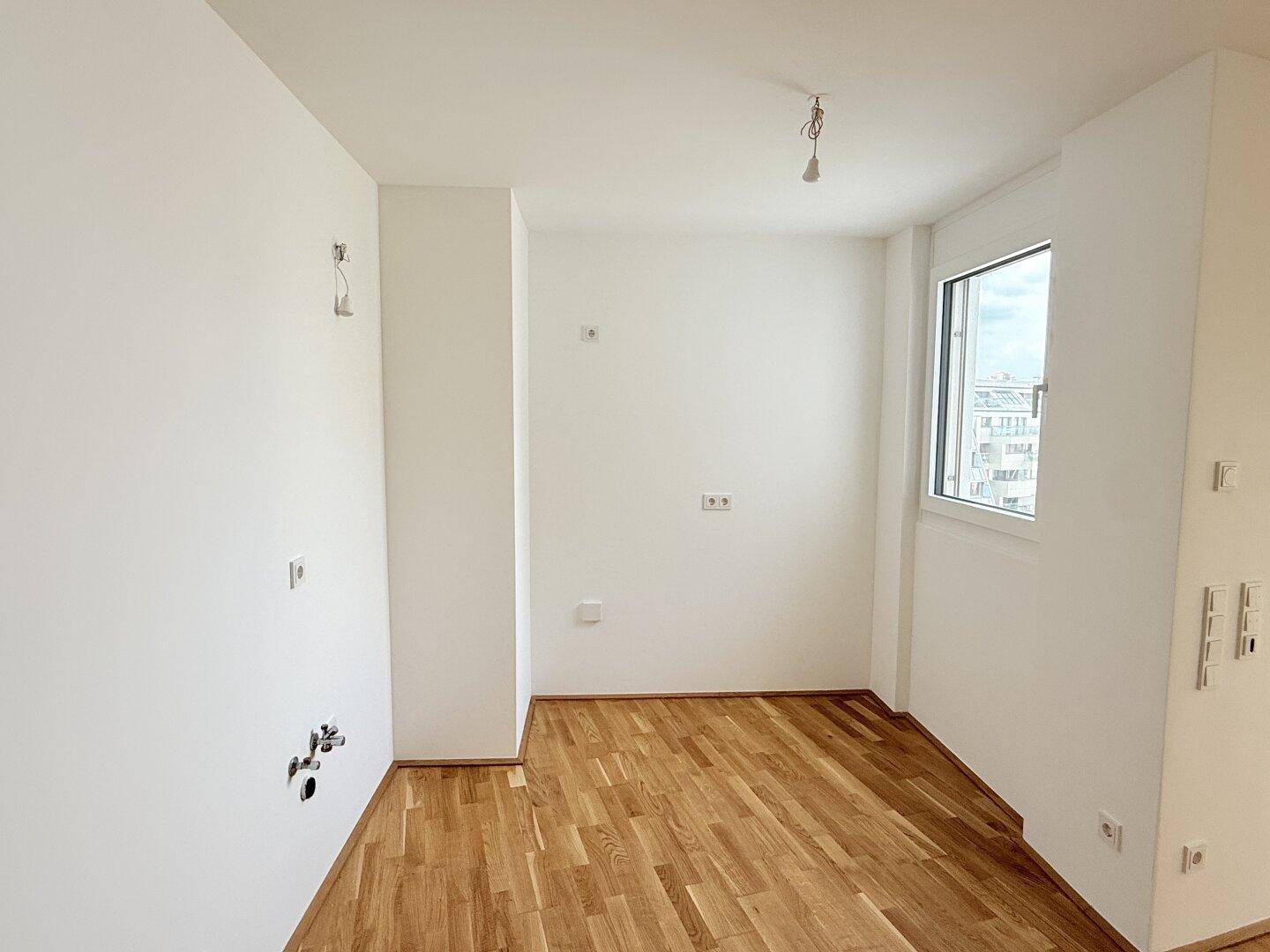 Leerer Küchenbereich mit Anschlüssen für Spüle und Geräte, bereit für eine Einbauküche.