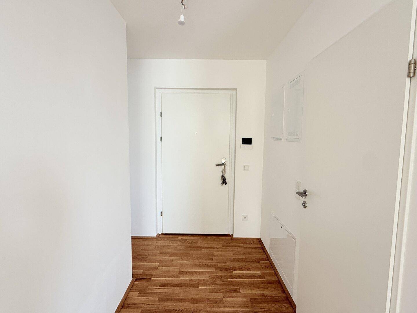 Heller Eingangsbereich mit Holzboden und weißer Tür, führt in die Wohnung.