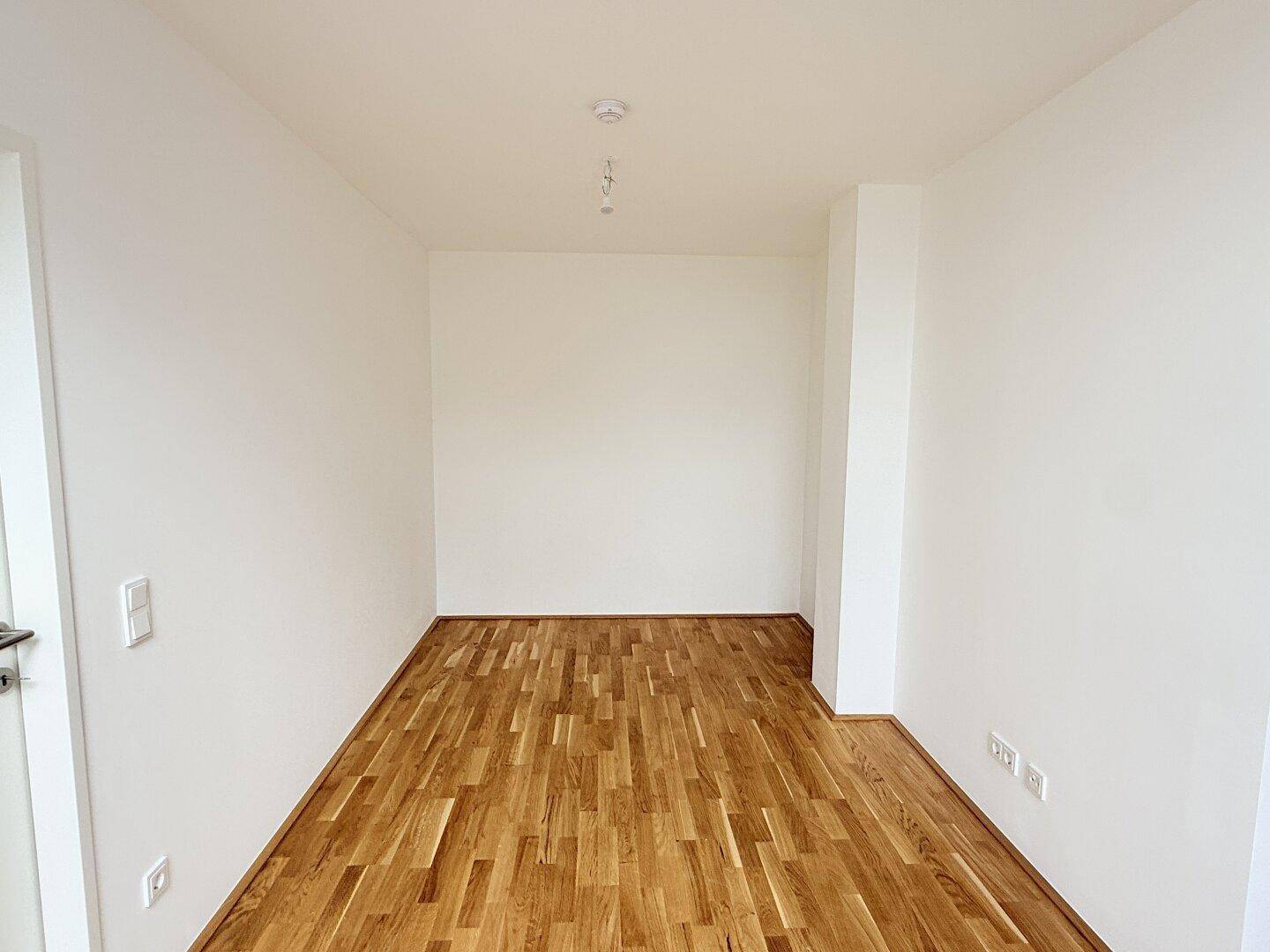 Leerer Raum mit weiß gestrichenen Wänden und warmem Holzparkett, bereit zur Einrichtung.