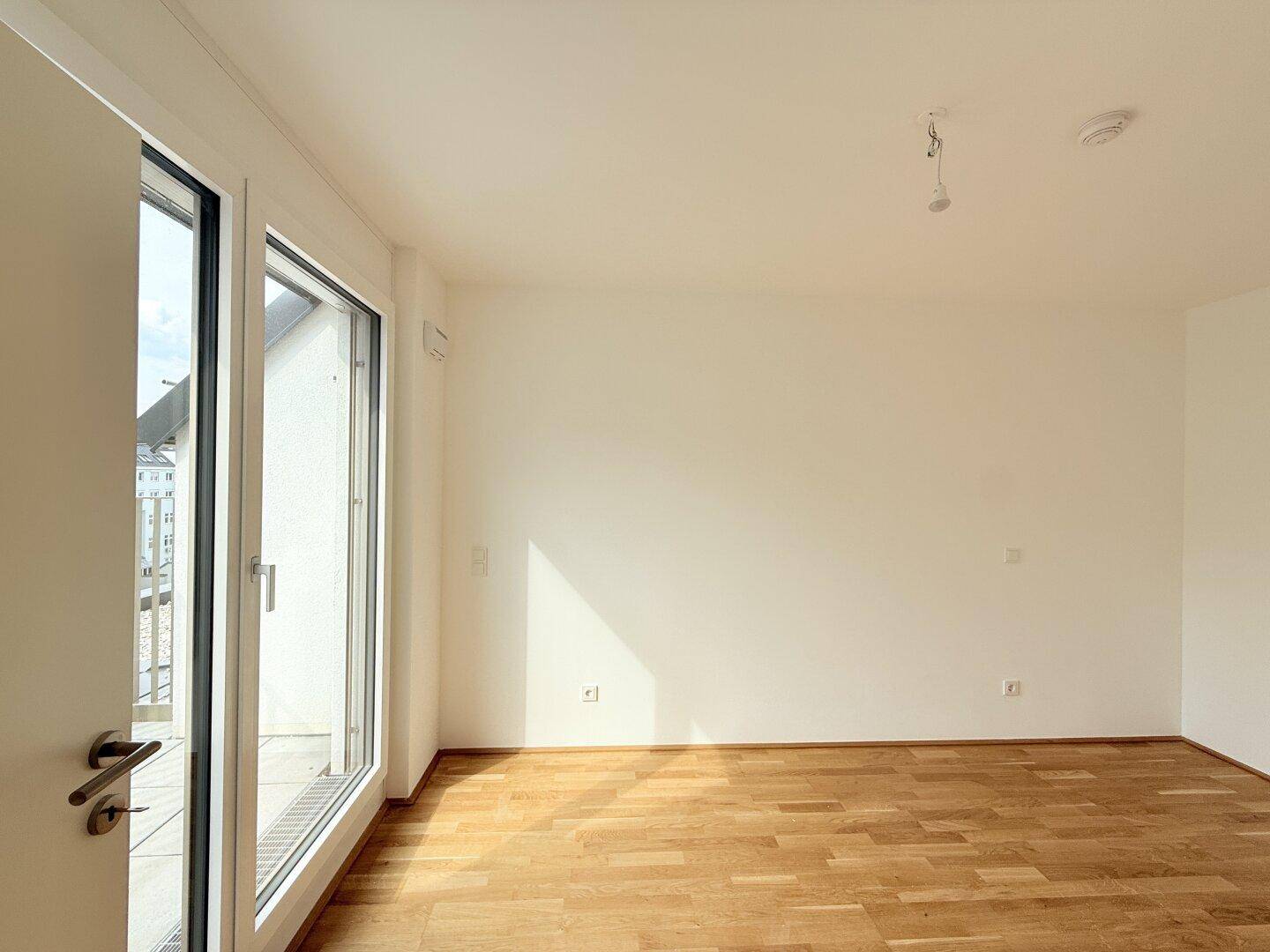 Heller Raum mit Zugang zu einem Balkon, ausgestattet mit neuem Parkettboden und weißen Wänden.