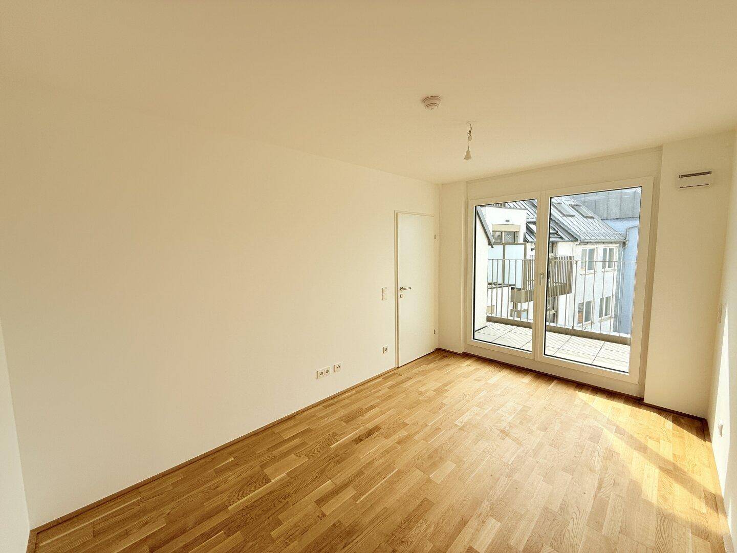 Geräumiger, heller Raum mit Parkettboden und großem Fenster mit Zugang zum Balkon.