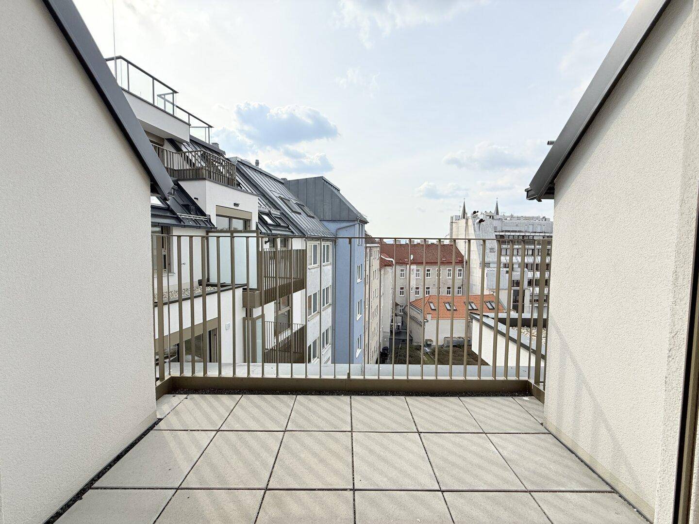 Geräumiger Balkon mit Fliesenboden und Metallgeländer, bietet Blick auf die Stadt.