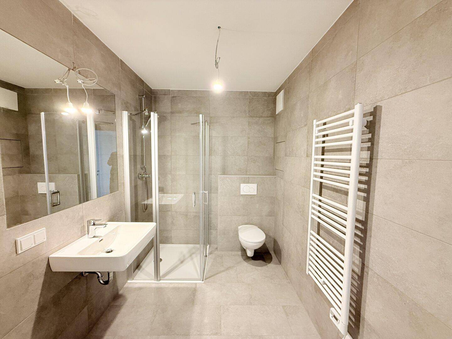 Zeitgemäßes Badezimmer mit Dusche, wandhängendem WC und beheiztem Handtuchhalter.