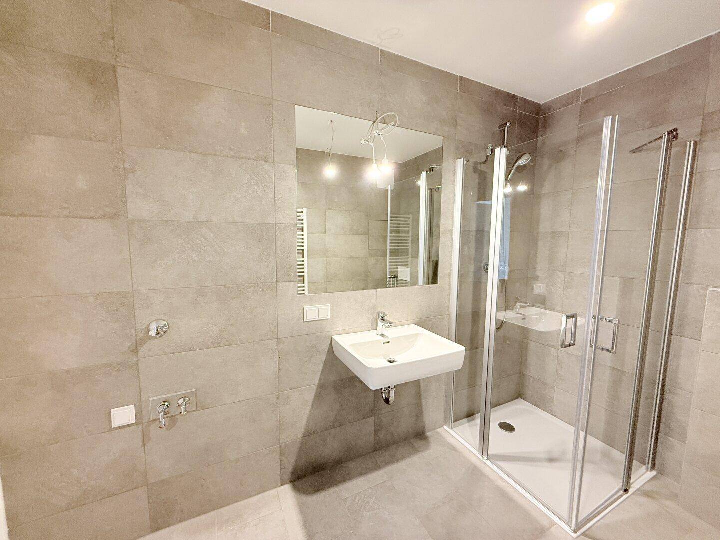 Modernes Badezimmer mit grauen Fliesen, Waschbecken und Duschkabine.
