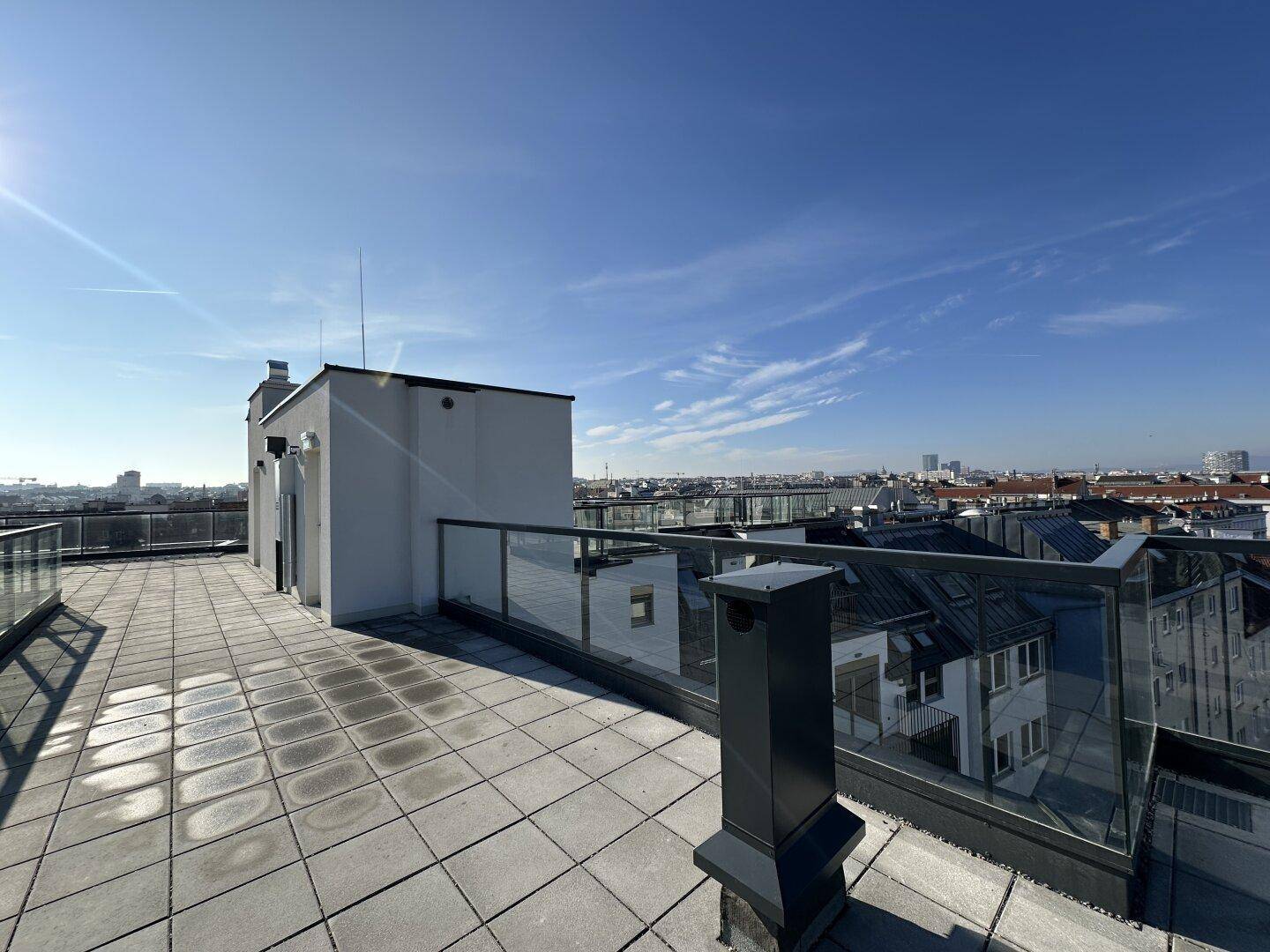 Große Dachterrasse mit Fliesen und Glasbrüstung, ideal für Entspannung mit Stadtblick.