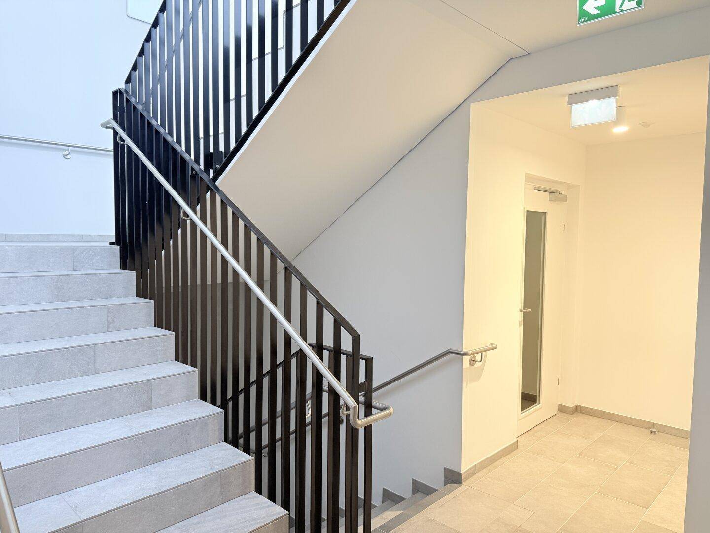 Modernes Treppenhaus mit Fliesenstufen und schwarzem Metallgeländer in einem Mehrfamilienhaus.