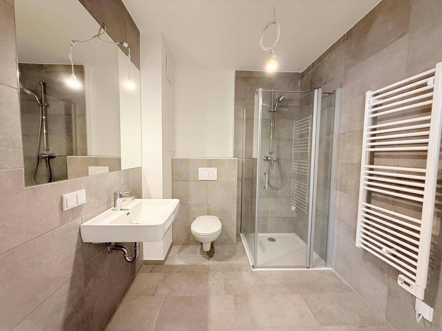 Modernes Badezimmer mit grauen Fliesen, Dusche, WC und beheiztem Handtuchhalter.