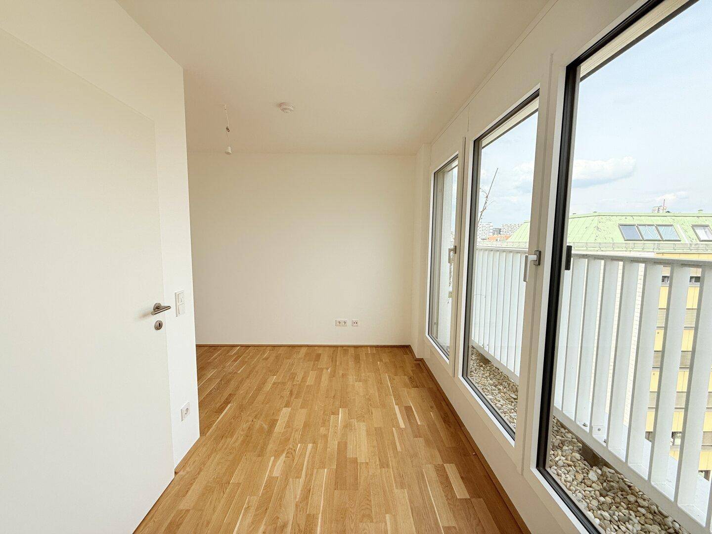 Schlafzimmer mit Parkettboden und Zugang zu einem französischen Balkon, bietet viel Tageslicht.