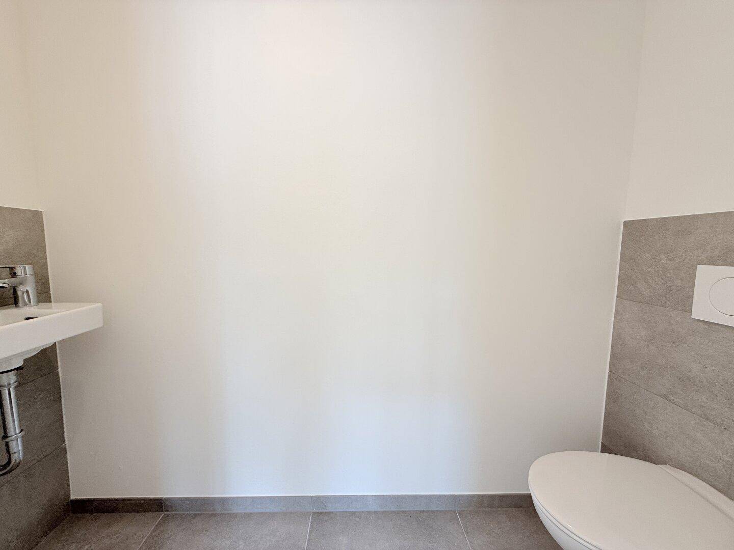 Modernes Gäste-WC mit Wand-WC, kleinem Waschbecken und grauen Fliesen an den Wänden.