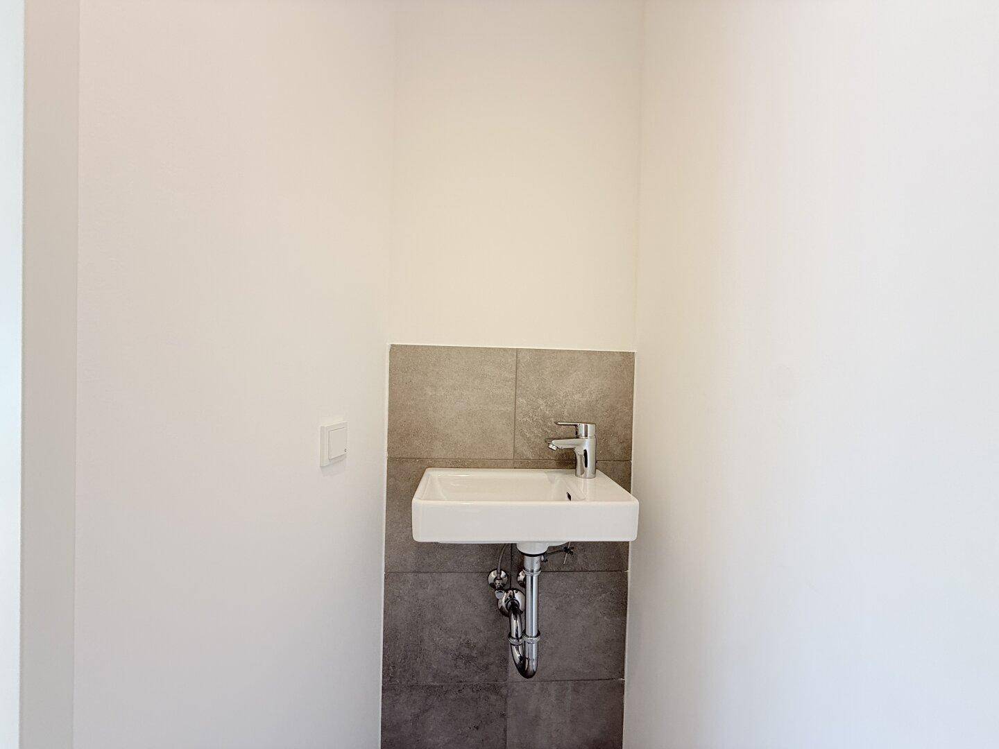 Kleines Waschbecken im Gäste-WC mit modernen Armaturen und grauen Wandfliesen.