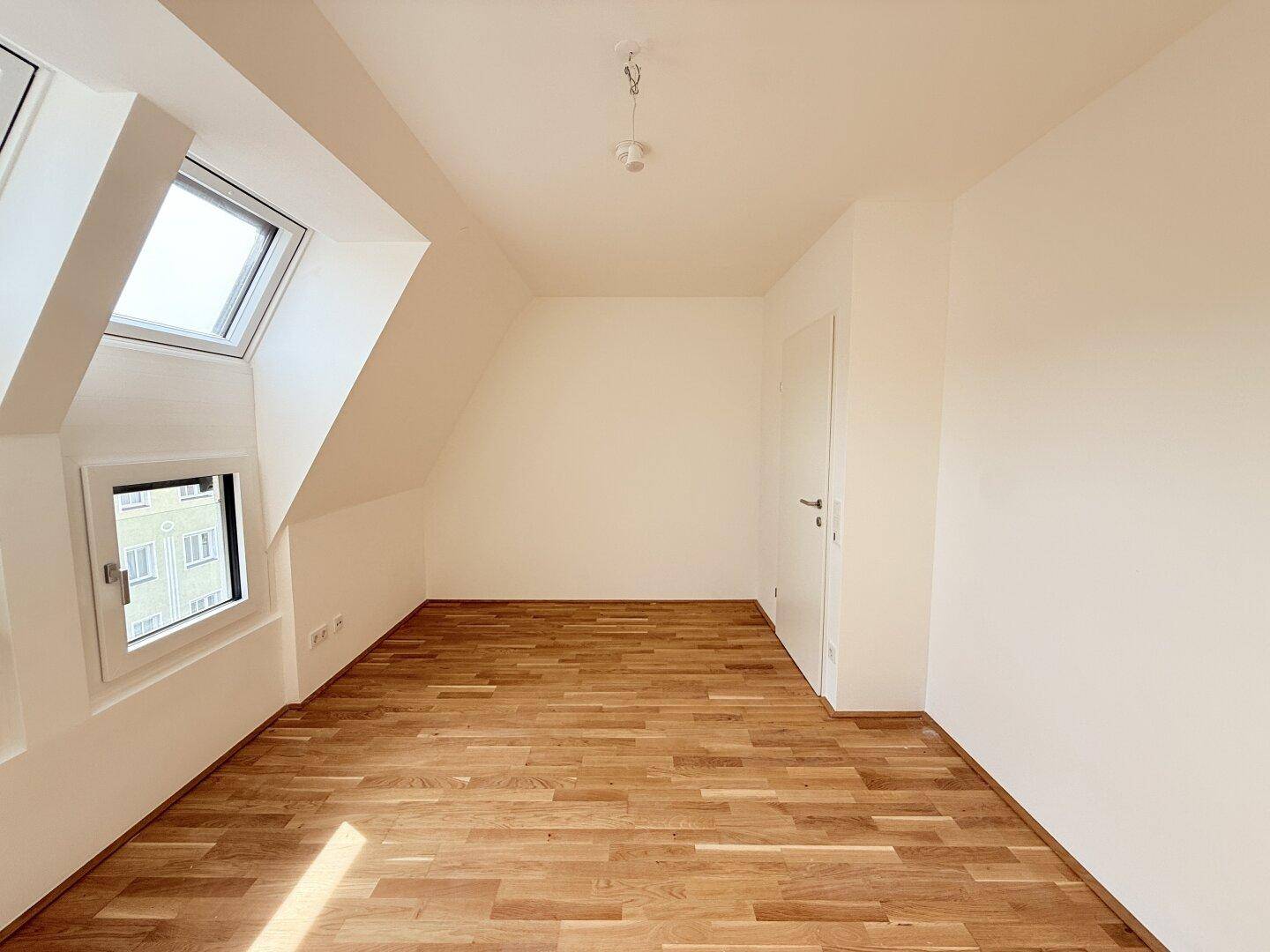 Dachgeschosszimmer mit Parkettboden und weiß gestrichenen Wänden, bietet eine gemütliche Atmosphäre.