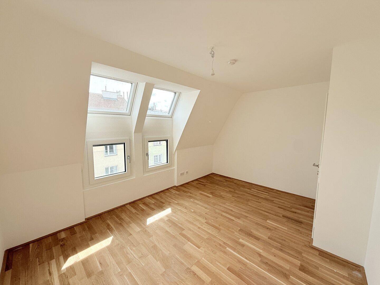 Heller Raum im Dachgeschoss mit Parkettboden und schrägen Wänden, ideal als Schlaf- oder Arbeitszimmer.