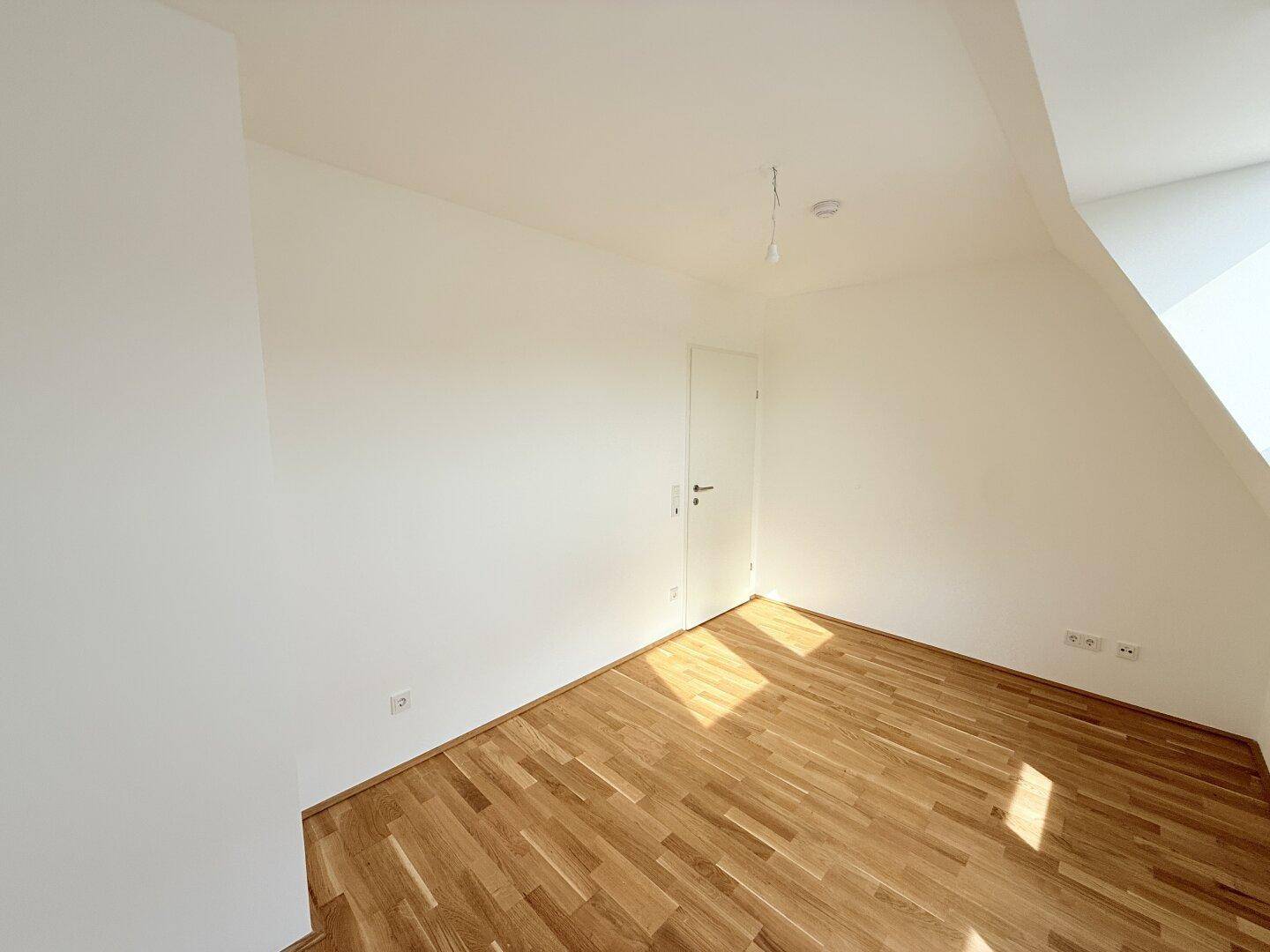Heller Raum im Dachgeschoss mit Parkettboden und schrägen Wänden, ideal als Schlaf- oder Kinderzimmer.