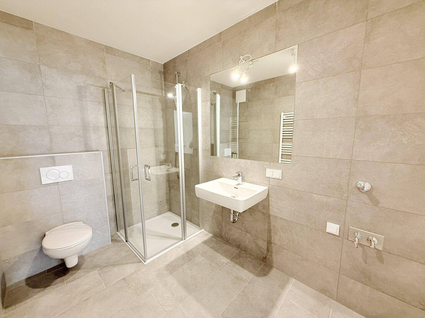Helles Badezimmer mit Duschkabine, Wand-WC und Waschbecken, ausgestattet mit modernen grauen Fliesen.