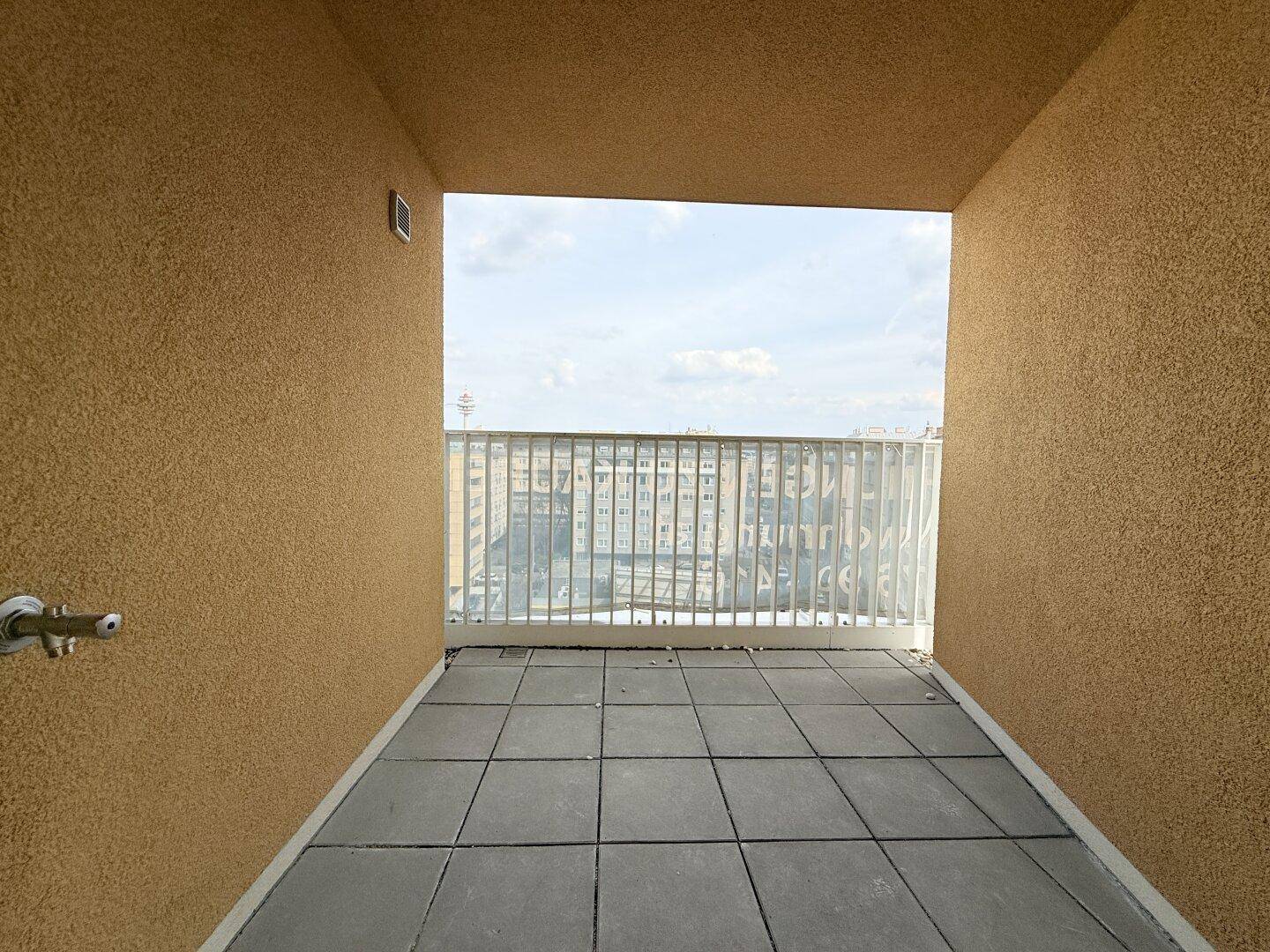 Überdachte Loggia mit Fliesenboden und Blick auf die Stadt, bietet einen geschützten Außenbereich.