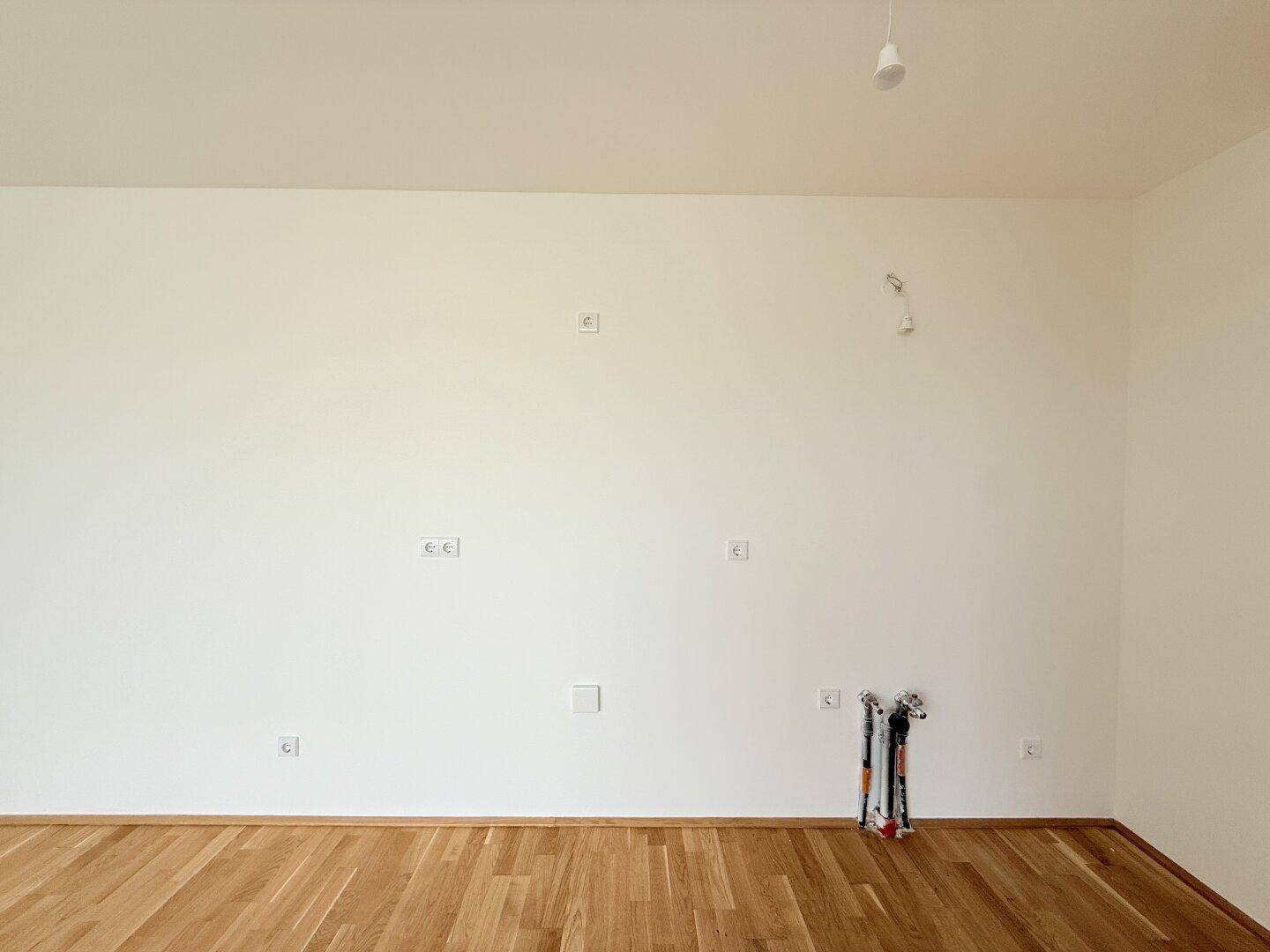 Detailansicht einer weißen Wand mit Steckdosen und Parkettboden in einem neuen Gebäude.